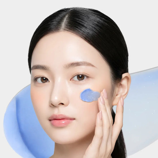 A woman applying a light blue cream (ISOV Azulene Care Cream) to her cheek.
