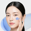 A woman applying a light blue cream (ISOV Azulene Care Cream) to her cheek.